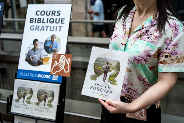 Prédication de rue d'un Témoin de Jéhovah avec présentoir de cours bibliques.