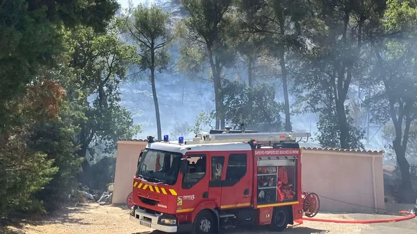 Camion de pompiers des Bouches-du-Rhône en zone boisée, fumée visible.