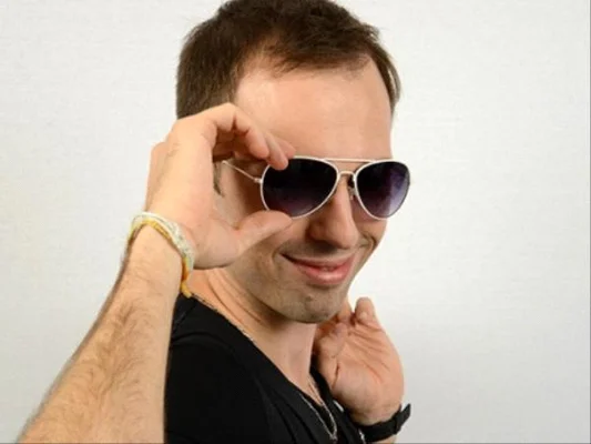 Victor Dixen tenant ses lunettes de soleil, souriant devant un fond blanc.