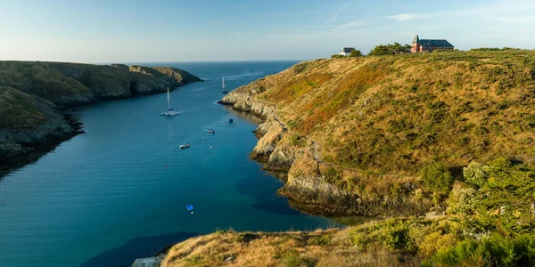 Crique paisible de Belle-Île-en-Mer avec voiliers et habitations sur les hauteurs.