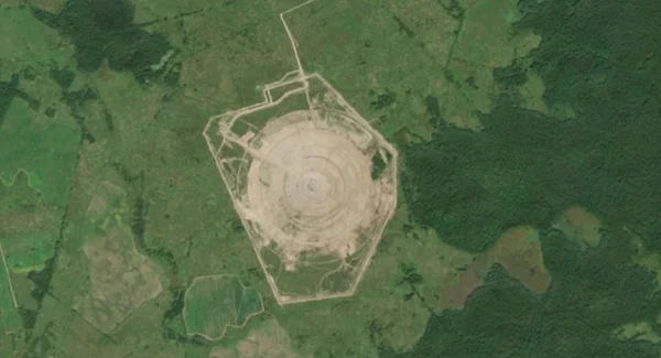 Photographie satellite d'un grand site d'excavation circulaire avec anneaux concentriques et clôture pentagonale.