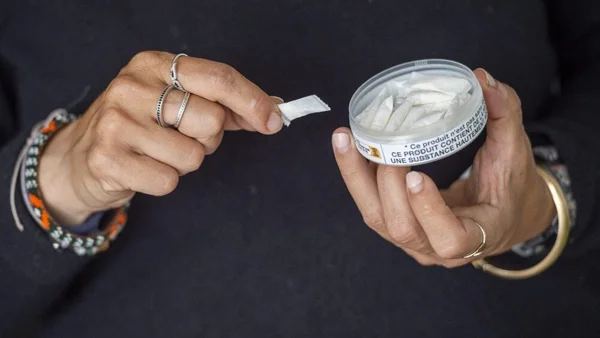 Personne manipulant une boîte de sachets de nicotine avec une étiquette d'avertissement sur l'addiction.