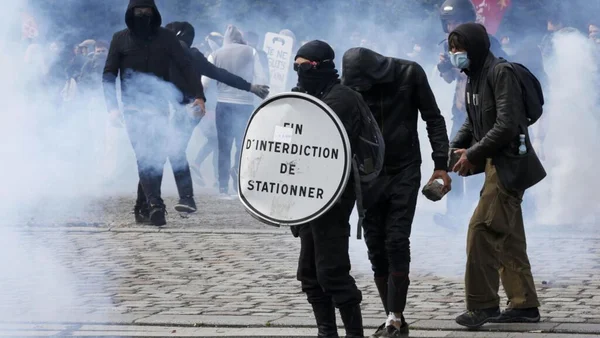 Manifestants de l'ultragauche affrontant les forces de l'ordre dans une rue enfumée.