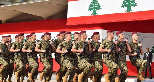 Défilé de soldats libanais en uniforme et béret rouge, drapeau national en arrière-plan.
