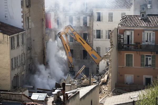 Une pelleteuse Liebherr réduit en poussière un immeuble endommagé à Marseille, sous un nuage de débris.