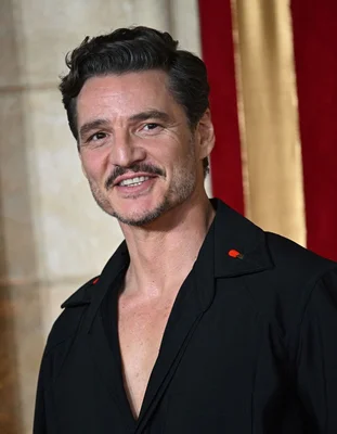 Portrait de Pedro Pascal souriant, vêtu d'une chemise noire à accents rouges.