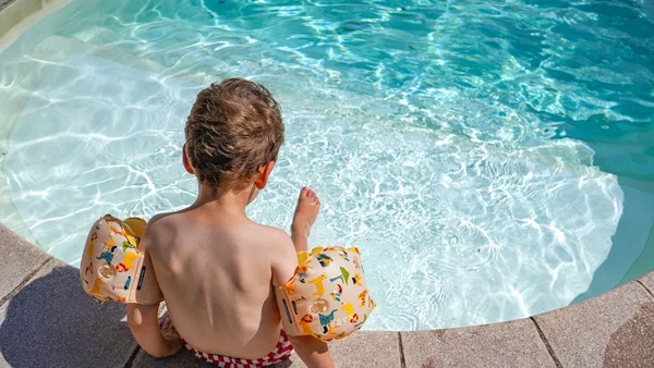 Jeune garçon au bord d'une piscine, équipé de brassards.