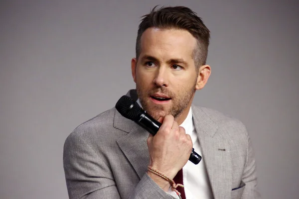 Ryan Reynolds en costume gris, micro à la main.