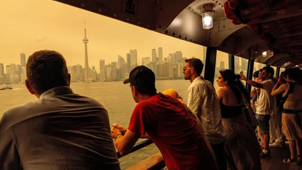 Des passagers sur un traversier observent la ligne d'horizon de Toronto plongée dans un brouillard orange, alors que la ville enregistre la pire qualité de l'air au monde.