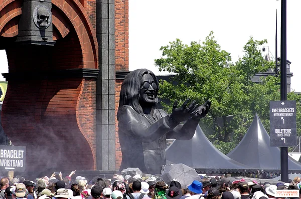 Statue géante noire sur la scène du Hellfest 2026, applaudissant devant une arche en brique, avec la foule en contrebas.