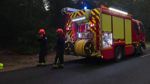 Deux pompiers de Seine-et-Marne près de leur véhicule, feux de détresse allumés, en pleine nuit.