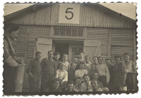 Hommes rassemblés devant une baraque numérotée dans un camp en 1942.