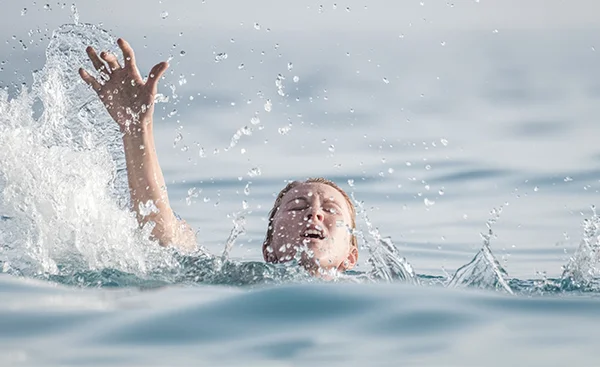 Personne en difficulté dans l'eau, un bras levé, illustrant un risque de noyade.