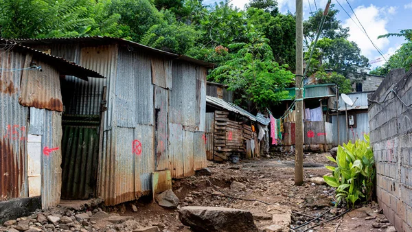 Vue d'une allée boueuse dans un bidonville, avec des habitations de fortune en tôle et bois, et du linge suspendu