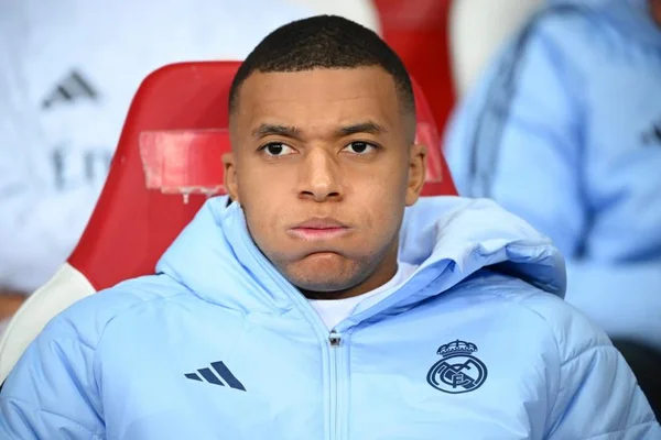 Kylian Mbappé assis sur un banc, vêtu d'une veste du Real Madrid.