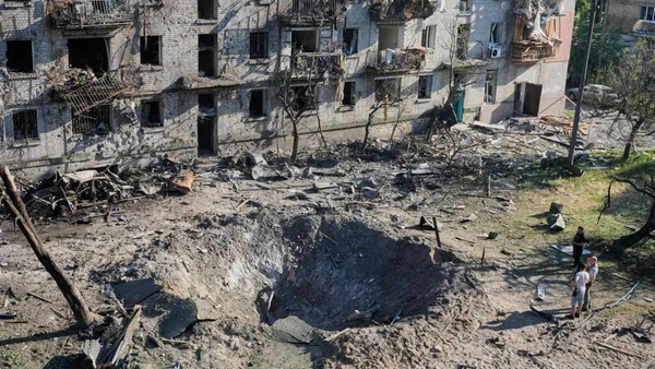 Un cratère d'impact et un immeuble résidentiel détruit à Kiev après une attaque russe massive, avec des civils observant les dégâts.