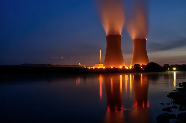 Tours de refroidissement d'une centrale nucléaire EDF illuminées au crépuscule, reflétées dans l'eau.