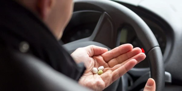 Un automobiliste tenant des pilules dans sa main, illustrant les risques liés à la conduite sous stupéfiants.