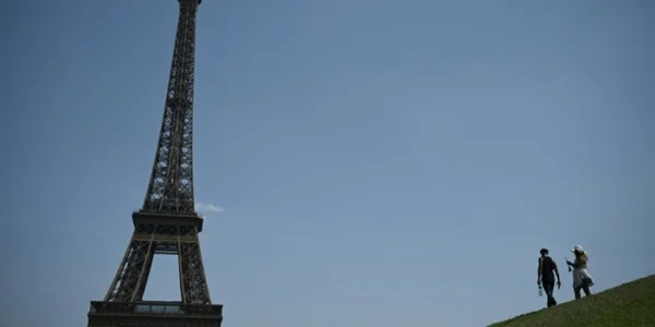 La tour Eiffel et des promeneurs gravissant une colline herbeuse.