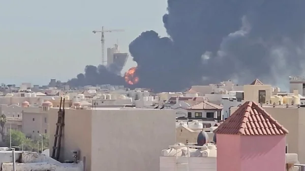 Explosion et fumée noire derrière une zone urbaine au Moyen-Orient, illustrant les tensions régionales.
