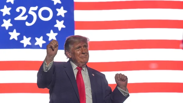 Donald Trump célèbre le 250e anniversaire des États-Unis, les poings levés devant un écran aux couleurs patriotiques.