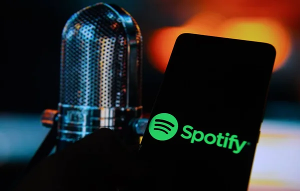 Smartphone avec logo Spotify devant un microphone vintage, fond flou chaleureux.