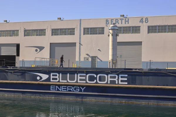 Barge « BLUECORE ENERGY » amarrée à un quai industriel « BERTH 48 », une personne se promène sur le ponton.