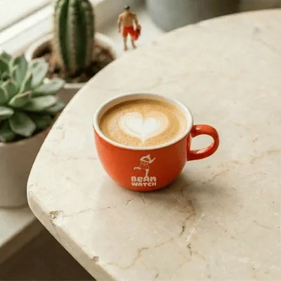 Un flat white dans une tasse orange, accompagné de plantes succulentes décoratives.