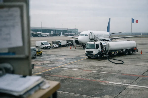 Un avion de ligne ravitaillé en carburant sur un tarmac d'aéroport, drapeau français visible en arrière-plan.