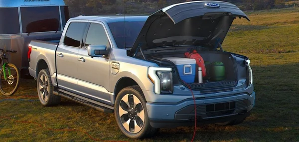 Ford F-150 Lightning argenté avec coffre avant ouvert et caravane.