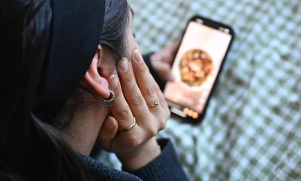 Personne utilisant un smartphone affichant une image de nourriture, sur fond flou.