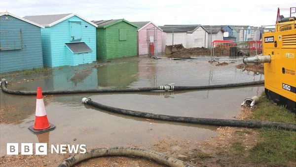Inondation près de cabanes de plage, évoquant les problèmes de gestion des eaux liés à Southern Water.
