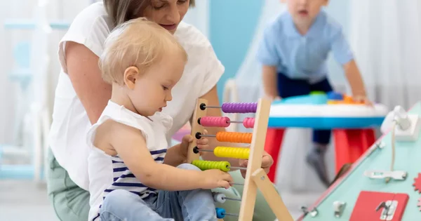 Une assistante maternelle jouant avec un enfant à l’aide d’un boulier en bois.