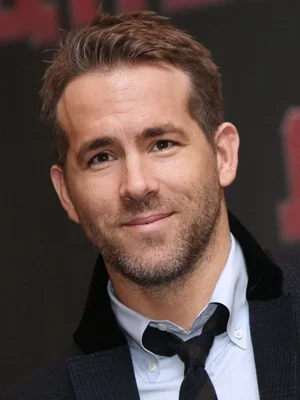 Ryan Reynolds dans un portrait rapproché, veste sombre et chemise bleue.