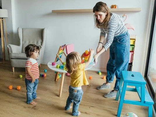 Une nounou jouant avec deux enfants dans un intérieur chaleureux.