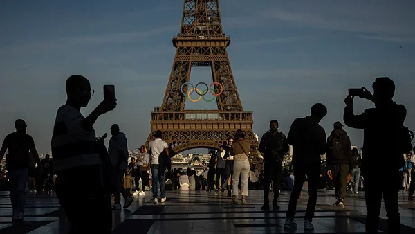 Touristes photographiant la tour Eiffel avec les anneaux olympiques, symbole des JO de Paris 2024.