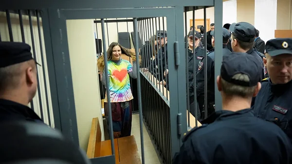 Une opposante antiguerre dans la cage des accusés, souriant malgré sa détention, entourée de policiers.
