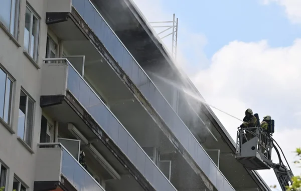 Pompiers en intervention sur un immeuble en feu à Anvers, arrosant les balcons depuis une nacelle.