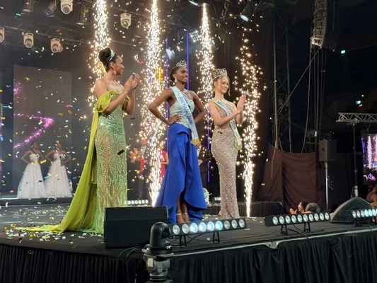 Sandra Justine (au centre) élue Miss Guyane 2026 sur scène, entourée de deux candidates, sous des effets pyrotechniques et des confettis.