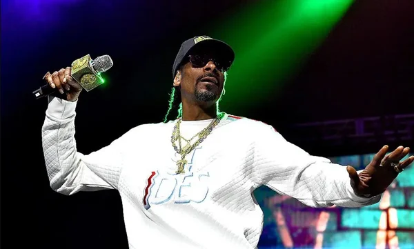 Snoop Dogg en concert, vêtu d'une chemise blanche et d'une casquette.