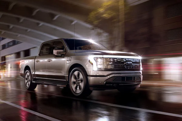 Ford F-150 Lightning argenté roulant de nuit sur une chaussée humide.