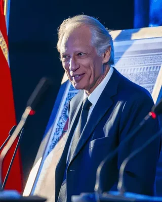 Dominique de Villepin prenant la parole à un pupitre, drapeau rouge en arrière-plan.