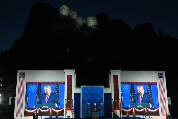 Meeting politique au Mont Rushmore : un orateur s'adresse à la foule devant les visages illuminés des présidents américains.