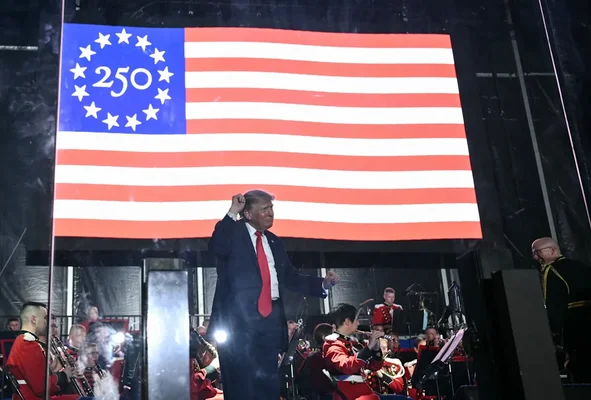Donald Trump, le poing levé, devant un écran géant aux couleurs du 250e anniversaire, avec des musiciens en uniforme.