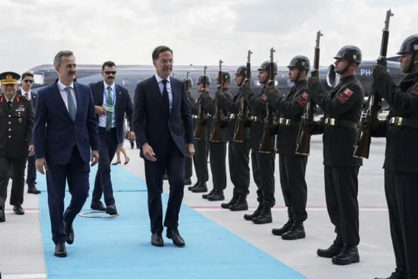 Arrivée de délégations au sommet de l'OTAN à Ankara : deux hommes en costume sombre défilent devant une garde d'honneur militaire sur le tarmac.