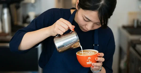 Une barista concentrée versant du lait chaud pour réaliser un latte art.