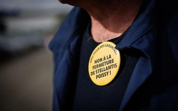 Un badge de protestation contre la fermeture de l'usine Stellantis de Poissy, porté par un salarié.