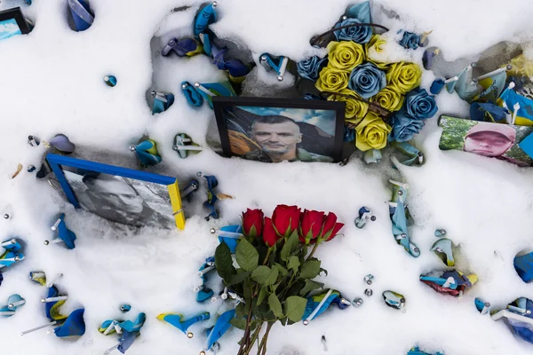 Mémorial enneigé à Kiev, Ukraine, le 24 février 2026, avec des portraits encadrés, des roses rouges et bleu-jaune et de nombreux petits drapeaux ukrainiens, au quatrième anniversaire de l'invasion à grande échelle.