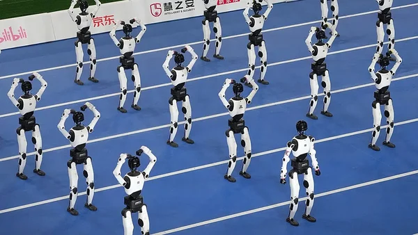 Robots humanoïdes sur la piste bleue lors de l'événement où un robot a battu le record du monde du 100 mètres d'Usain Bolt, exécutant une routine synchronisée avec bras levés, bannières Bilibili et JD.com en fond.