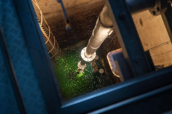 Vue plongeante sur le captage d'eau potable de Fraise-Bois Boulard à Vérines, en Charente-Maritime : un puits cylindrique profond contenant un liquide vert et une grande conduite métallique descendante.